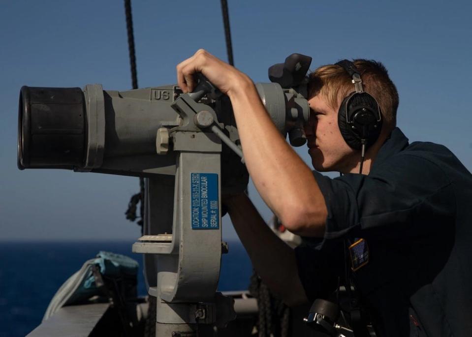 A photo of a man looking through binoculars on the USS Gerald R. Ford.
