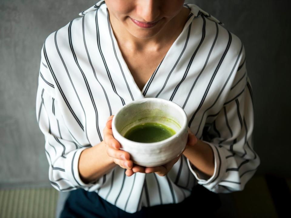 A woman holds a mug of green tea.