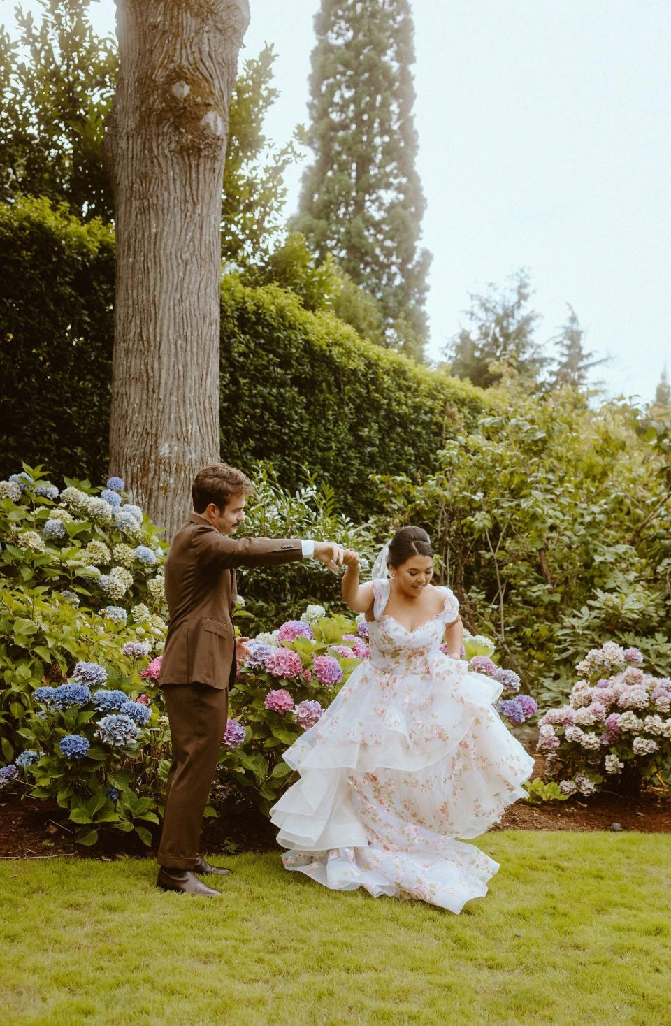 A groom spins a bride in a garden.