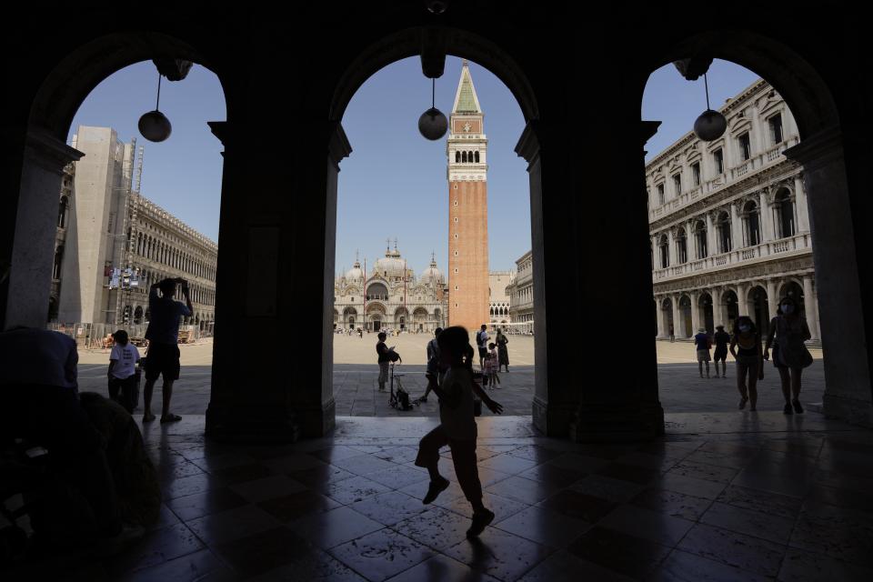 People are backdropped by St. Mark's bell tower, in Venice, Italy, Thursday, June 17, 2021. After a 15-month pause in mass international travel, Venetians are contemplating how to welcome visitors back to the picture-postcard canals and Byzantine backdrops without suffering the indignities of crowds clogging its narrow alleyways, day-trippers perched on stoops to imbibe a panino and hordes of selfie-takers straining for a spot on the Rialto Bridge or in front of St. Mark’s Basilica. (AP Photo/Luca Bruno)