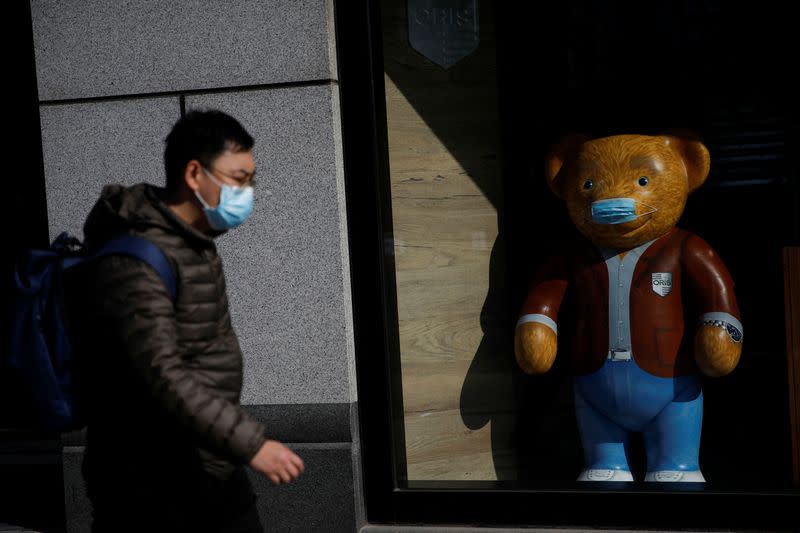 A man wearing a face mask walks past a bear doll, following an outbreak of the coronavirus disease (COVID-19), in Beijing, China
