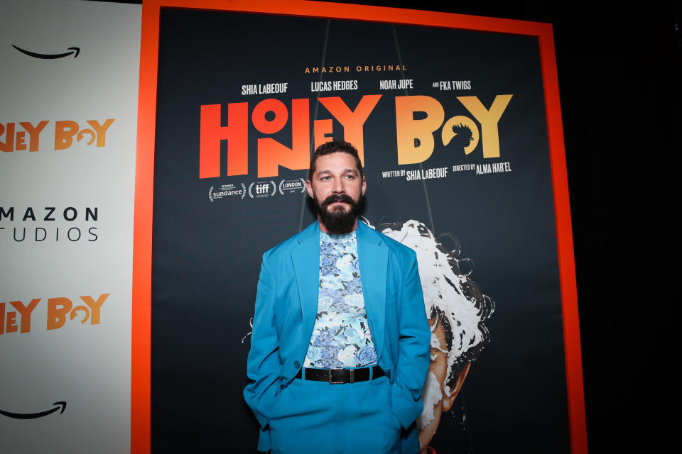 Shia standing in front of a poster for Honey Boy