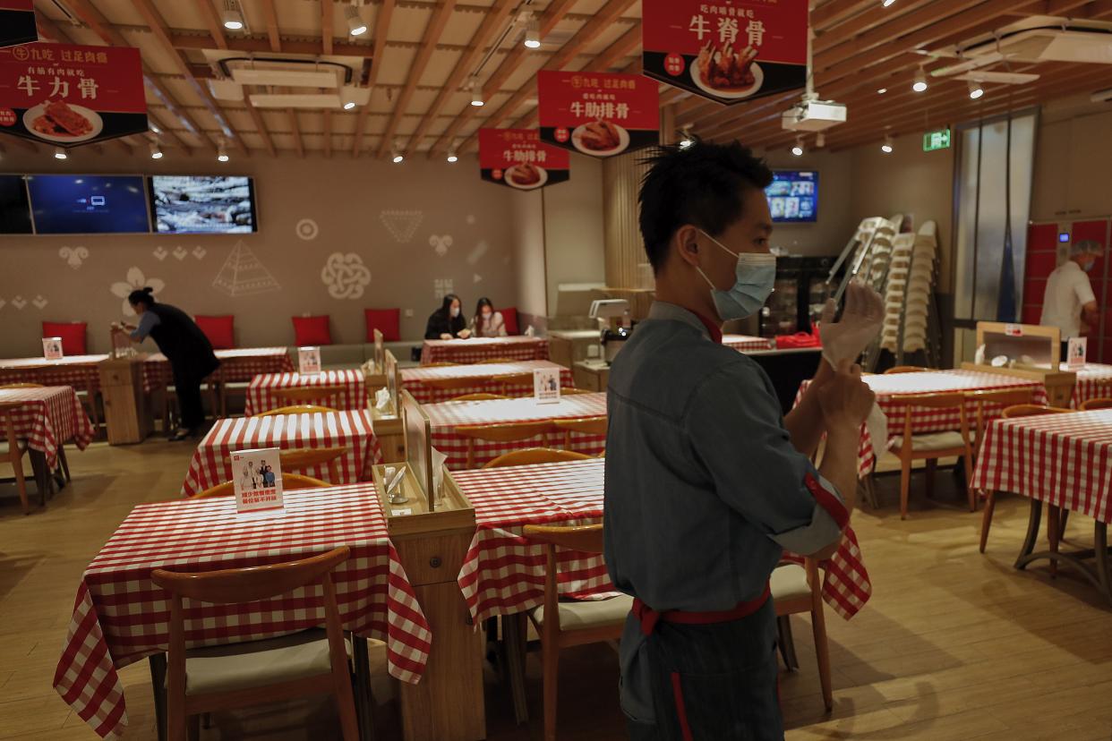 A worker wearing a protective face mask puts on gloves to prevent the spread of the coronavirus as he prepares to serve customers at the Xibei restaurant in Beijing on March 24, 2020.