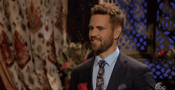 Nick from the "Bachelor" with a rose in hand, smiling and nodding in an animated manner