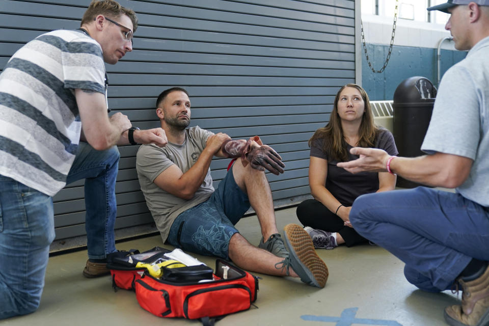 While Lucas Drake, center, plays a victim of an accident, an instructor goes over their response to the simulated incident during a Global Wind Organisation certification class at the Massachusetts Maritime Academy in Bourne, Mass., Thursday, Aug. 4, 2022. At the 131-year-old maritime academy along Buzzards Bay, people who will build the nation's first commercial-scale offshore wind farm are learning the skills to stay safe while working around turbines at sea. (AP Photo/Seth Wenig)