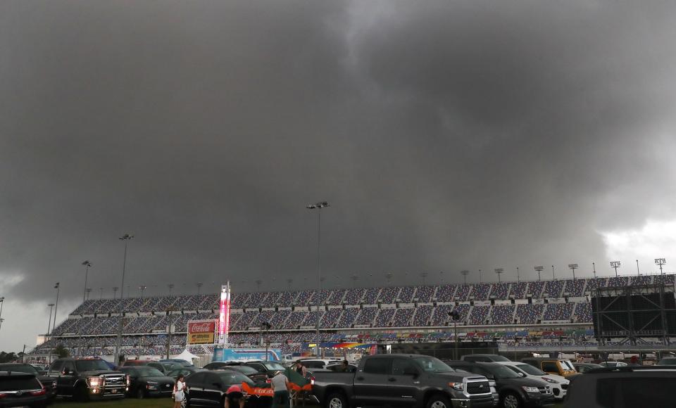 Fans head for cover in the infield parking area as one of the new LED scoring pylons at Daytona International Speedway flashes a weather alert on Saturday at the Coke Zero Sugar 400 at Daytona International Speedway. The rain-delayed race generated an unanticipated boost in food and beverage sales at some Daytona Beach hotels.