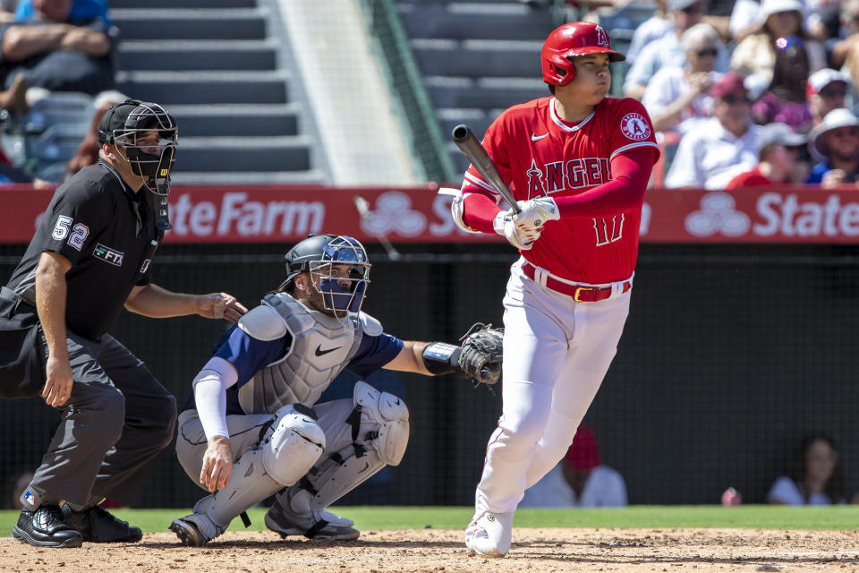 Los Angeles Angels designated hitter Shohei Ohtani, right, follows through on a single to right field next to Seattle Mariners catcher Curt Casali, center, and home plate umpire Jansen Visconti, left, during the third inning of a baseball game in Anaheim, Calif., Sunday, Sept. 18, 2022. (AP Photo/Alex Gallardo)