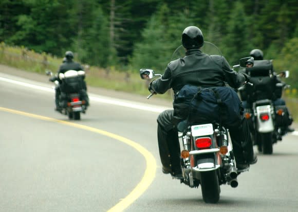 Three motorcycles being ridden by leather-clad men on the highway.