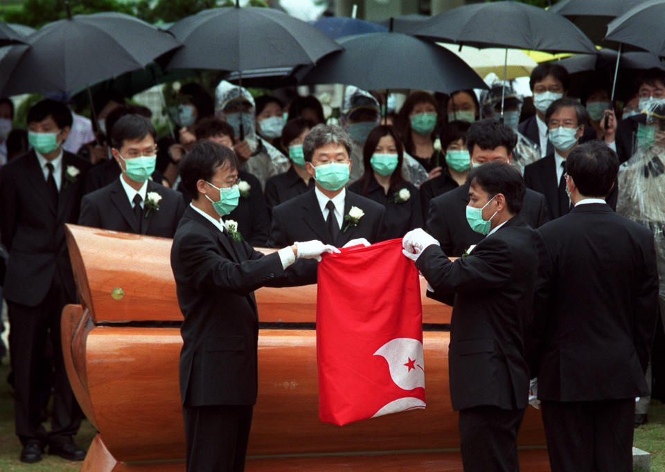 Mourners wearing surgical masks to protect against SARS virus, fold the Hong Kong flag above the coffin of Lau Kam-yung, 27, a frontline health worker killed by SARS, during a funeral service in Hong Kong Monday, June 9, 2003. (Lo Sai Hung/AP)