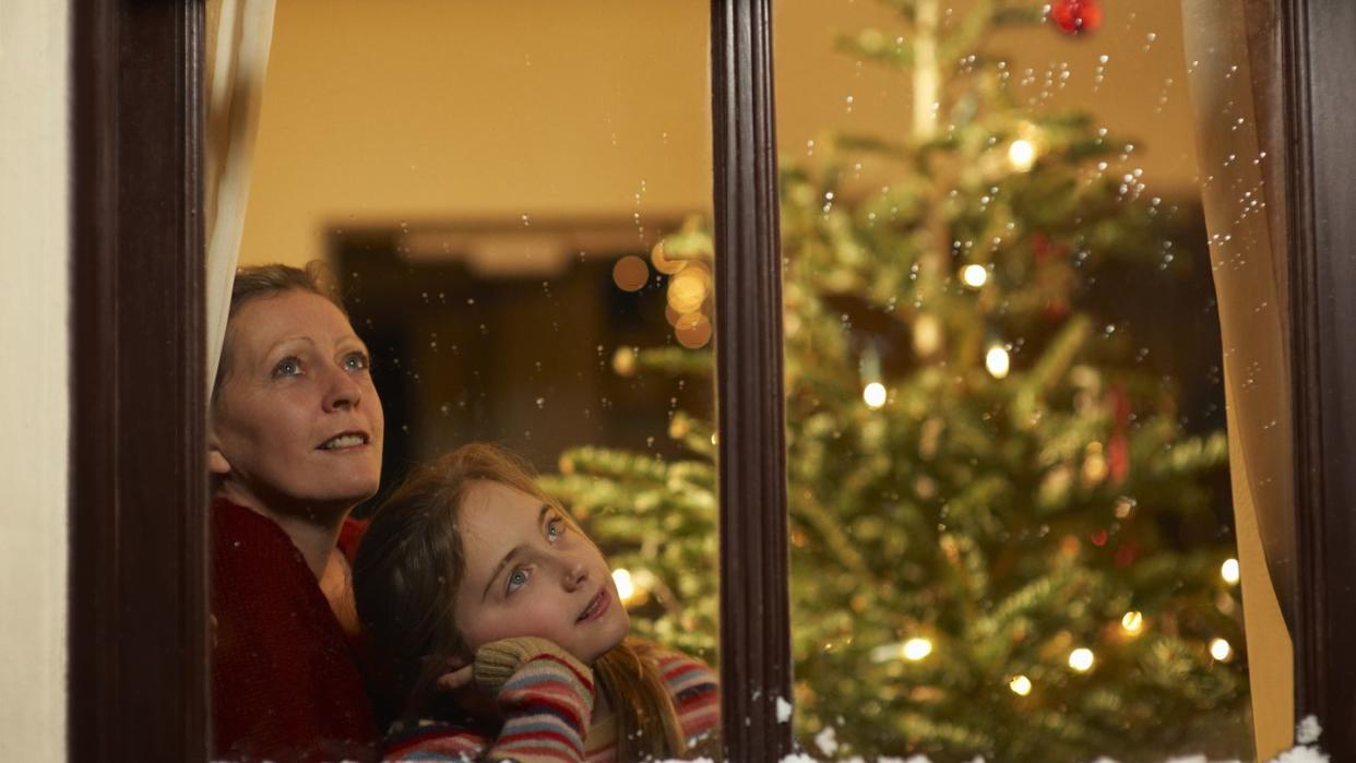 girl and mother gazing out of window at christmas