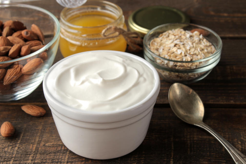 Greek yogurt in a ceramic bowl with almonds and honey, oatmeal next to a spoon on a brown wooden background. healthy food. natural yoghurt. breakfast.