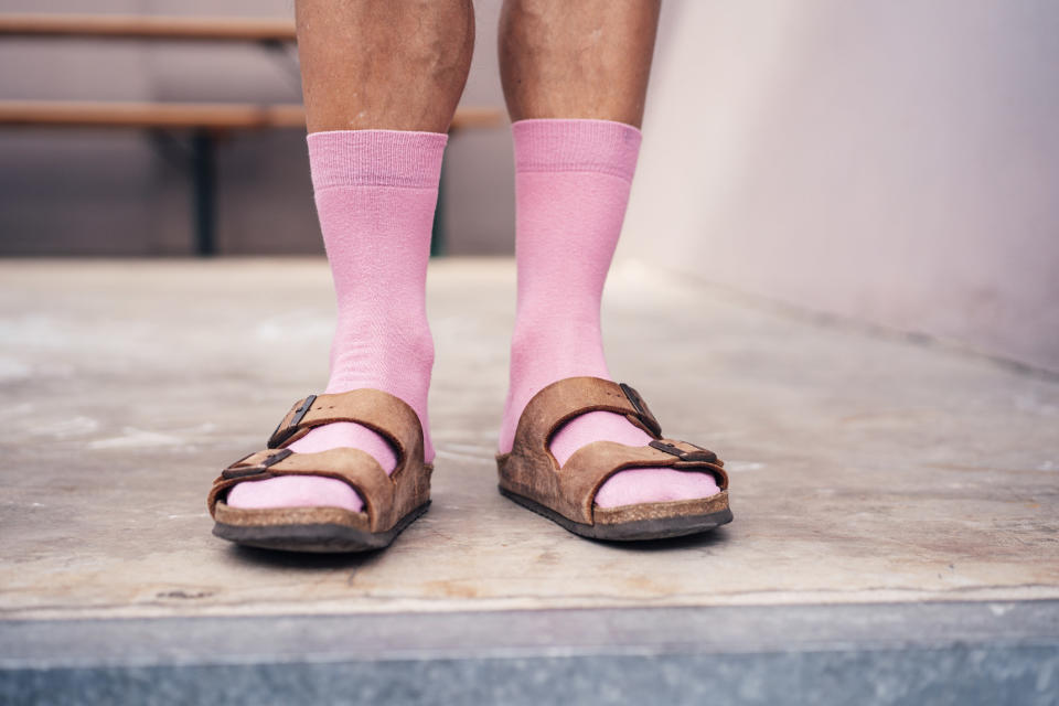 Person wearing a combination of pink socks and brown sandals. The person's lower legs are visible