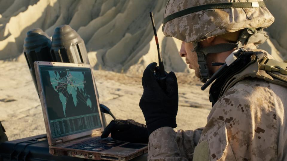 A soldier uses a laptop on a field mission in a desert.