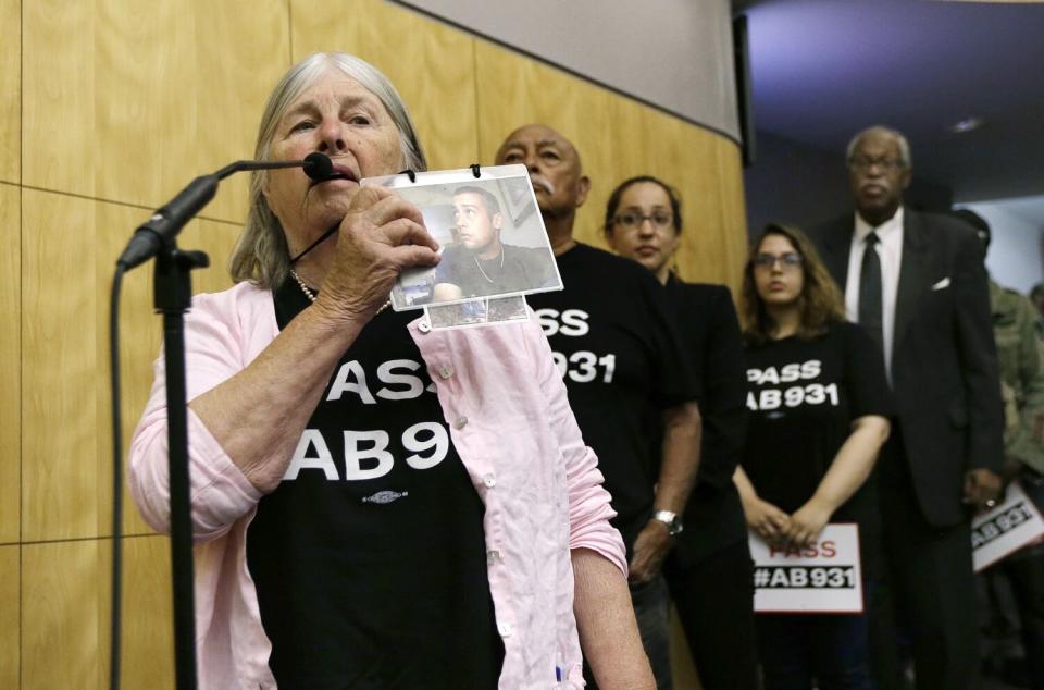 A woman at a microphone holding a photograph of her slain son