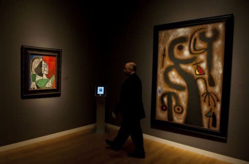 A guard walks by Joan Miro's "Peinture" (R) and Pablo Picasso's "Femme Assise Sur Fond Bleu-Rouge" during a press preview for Sotheby's Masters Auction in New York. The auction of Impressionist and Modern art will take place on May 2