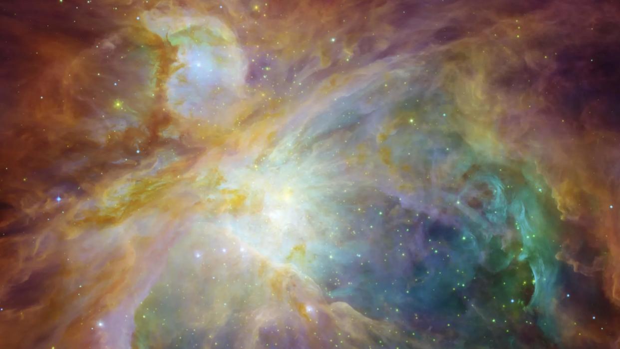  A Hubble Space Telescope image of the Orion Nebula shows swirling clouds of orange, blue, white and green dust in a field of twinkling stars. 