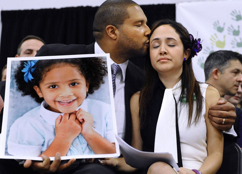 Jimmy Greene, left, kisses his wife Nelba Marquez-Greene as he holds a portrait of their daughter, Sandy Hook School shooting victim Ana Marquez-Greene, at a news conference in Newtown, Conn. in 2013