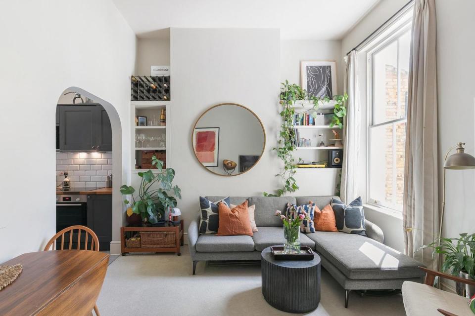 a living room with a couch and a mirror and a wine rack to the left and the kitchen to the left