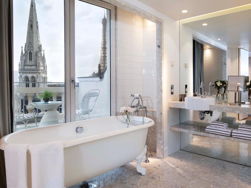 A hotel bathroom with a standing tub and views of the city outside the window, including the Eiffel Tower.