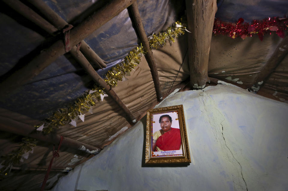 A portrait of Padmavathi, who died of COVID-19, hangs on the wall of her family hut made from bamboo and plastic sheeting in a slum in Bengaluru, India, Thursday, May 20, 2021. Padmavathi collected hair, taking it from women's combs and hairbrushes to later be used for wigs. She earned about $50 a month. (AP Photo/Aijaz Rahi)