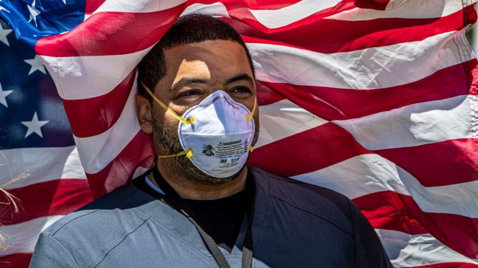 Hombre con mascarilla y bandera de EE.UU. detrás.