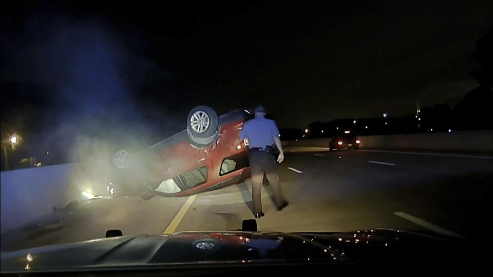 This screen shot taken from dash cam video owned by the Arkansas State Police shows trooper Rodney Dunn walking toward a flipped car in Pulaski County, Ark., on July 9, 2020. An Arkansas woman is suing the state police after she says a trooper crashed into her car, causing it to flip, after she didn't immediately pull over for a traffic stop. An attorney for Janice Nicole Harper filed the lawsuit last month, May 2021, in Pulaski County against trooper Rodney Dunn and the Arkansas State Police. (Arkansas State Police via AP).