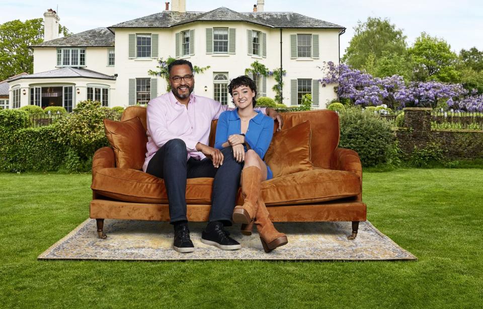 father and daughter martin and jess from my mum, your dad, smiling while sitting on a burnt orange couch in front of a country estate