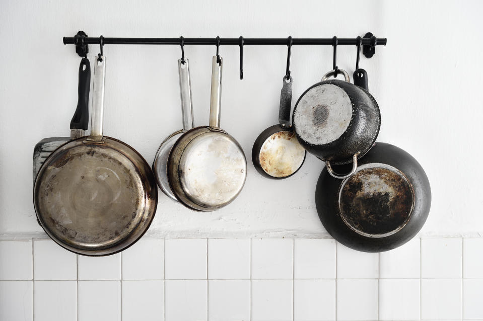 Five used frying pans hanging on a kitchen wall rack