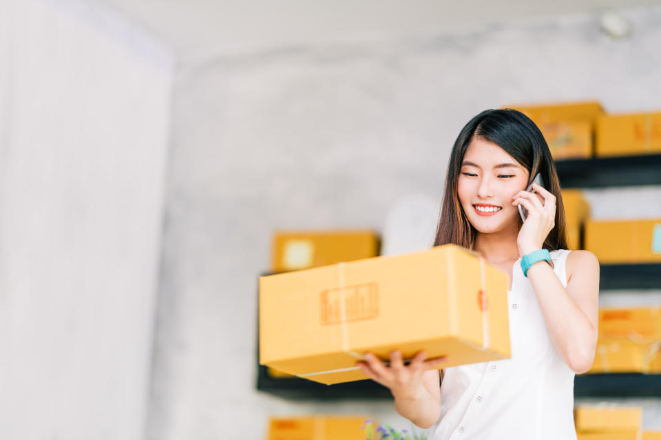 A smiling woman holds up a box and talks on her cell phone.