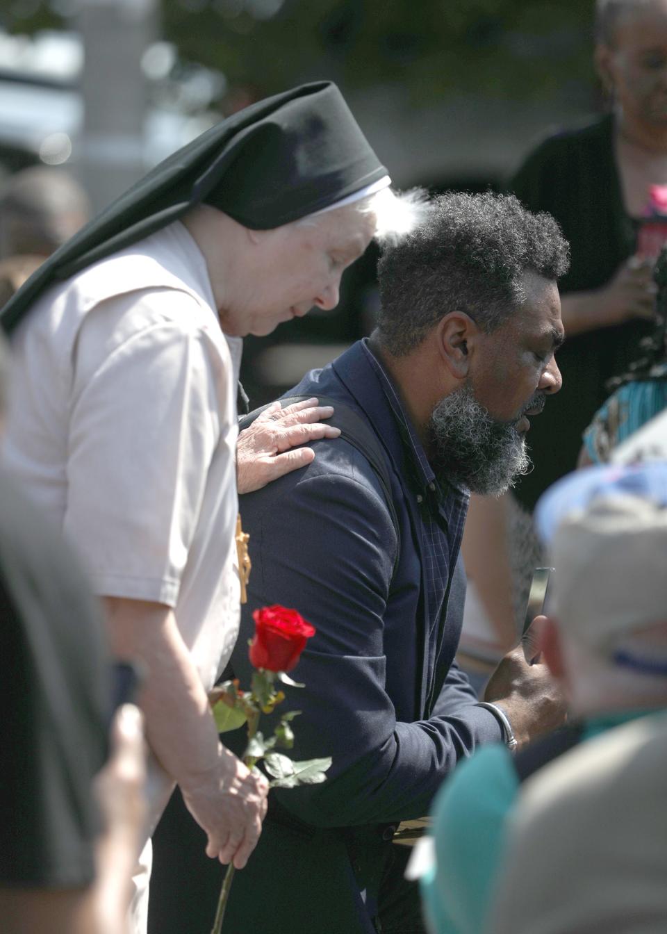 Family and community members come out to pray and be together in the street in front of the Tops Friendly Market on Jefferson Ave., in Buffalo, NY on May 15, 2022.  Dewitt Lee III  offers a prayer to the group while a woman holding a rose touches him. Ten people were killed and three others injured in a shooting at the Buffalo grocery store on May 14, 2022.