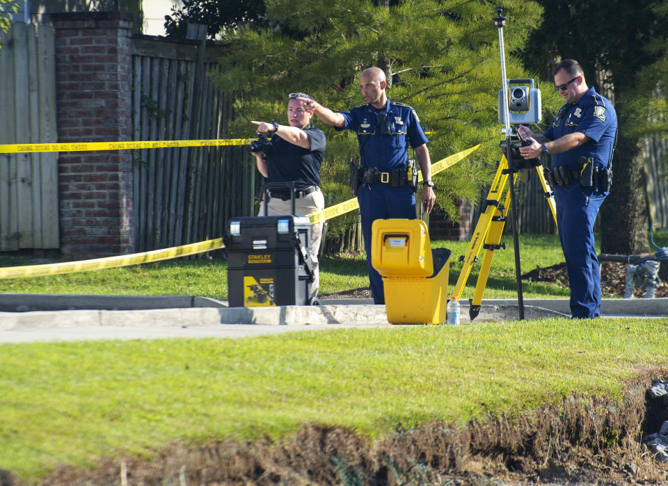 Louisiana State Police talk as they document evidence near crime scene markers in the parking lot of the Willowbrook Center shopping area at Hoo Shoo Too Road and Jefferson Highway, Saturday, Oct. 9, 2021, in Baton Rouge, La., after a suspect exchanged fire near there with an LSP trooper earlier in the day. (Travis Spradling/The Advocate via AP)
