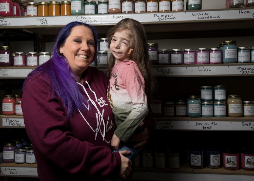 Kriss Schmitt holds her daughter, Kailey, in front of her inventory of homemade candles on Feb. 15 at her home in Marshfield.