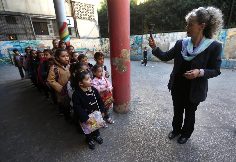 In this picture taken on Wednesday, March 5, 2014, a Lebanese teacher Hanan Khattar, right, ring the bill as Syrian refugee students line up to enter their classroom at a Lebanese public school in Beirut, Lebanon. More than 2 million of those who should be in school remain in Syria, where classrooms have been bombed, used as shelters or turned into military barracks. Another 300,000 Syrian children don’t attend school in Lebanon, along with some 93,000 in Jordan, 78,000 in Turkey, 26,000 in Iraq and 4,000 in Egypt, UNICEF officials in Geneva said. Those numbers likely are higher, as UNICEF can’t count the children whose parents didn’t register with the United Nations refugee agency. (AP Photo/Hussein Malla)