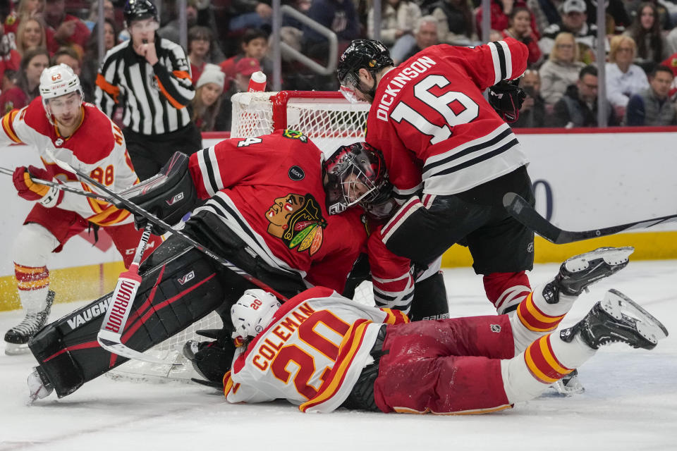 Chicago Blackhawks goaltender Petr Mrazek, top center, sits on the puck as Calgary Flames center Blake Coleman (20) dives on the ice while trying to shoot during the second period of an NHL hockey game Sunday, Jan. 7, 2024, in Chicago. (AP Photo/Erin Hooley)