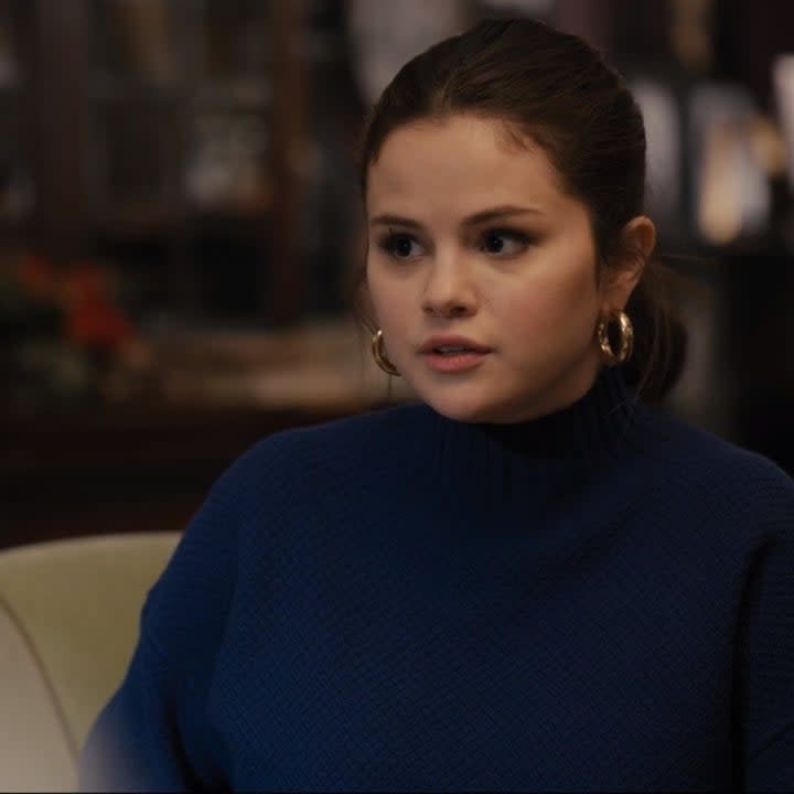 Photo of Selena Gomez as Mabel in a blue sweater, gold accessories, and pink lipstick