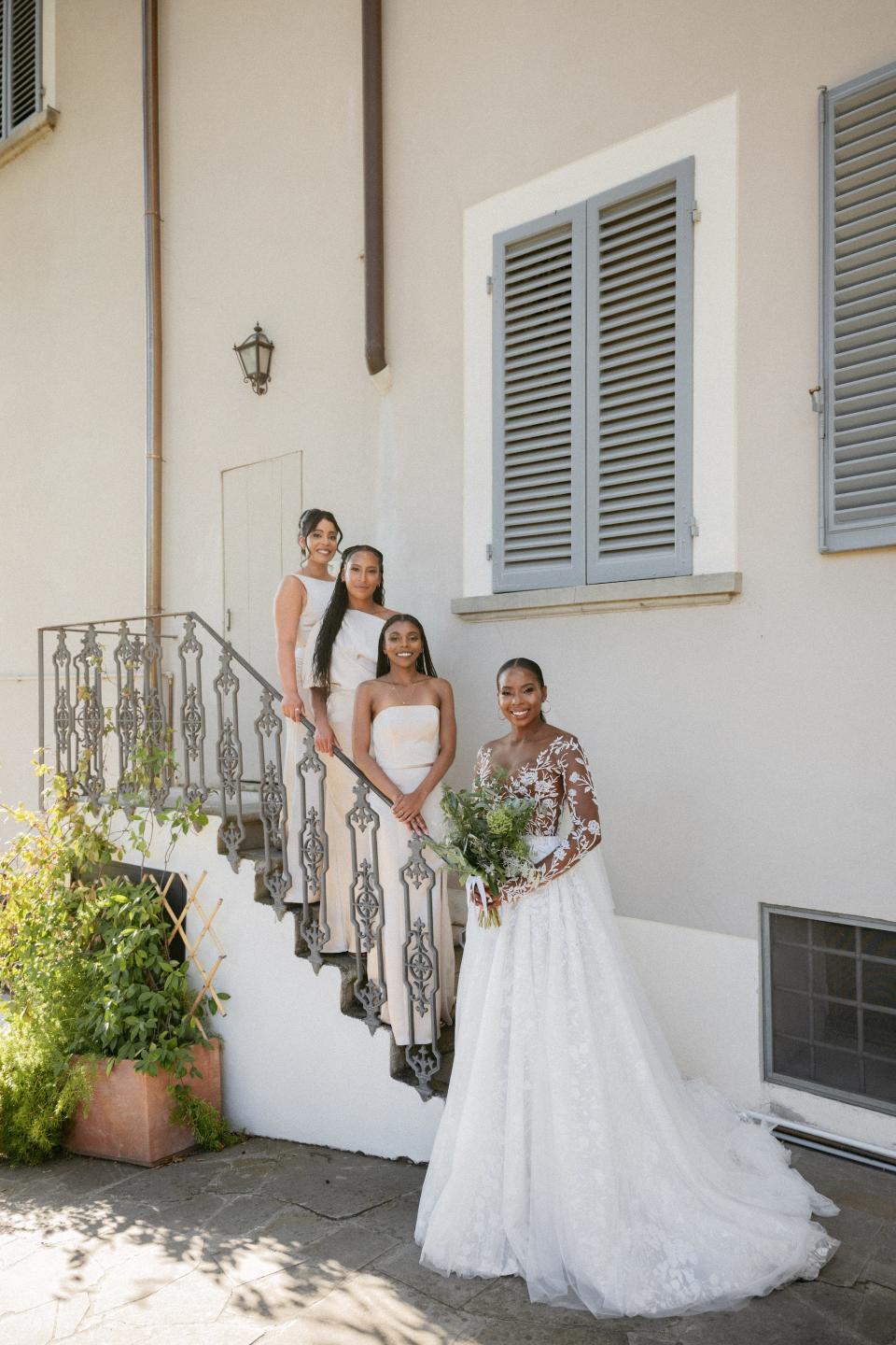 A bride stands in front of her bridesmaids, who pose on a staircase on the outside of a building.