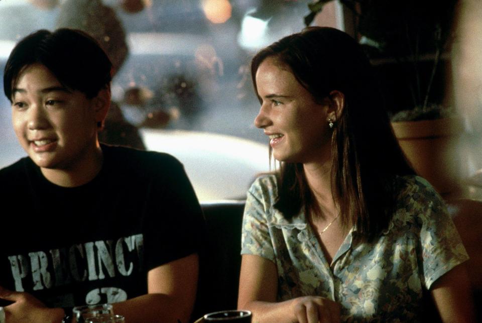 Ernest Liu & Juliette Lewis smile as they sit next to each other at a diner