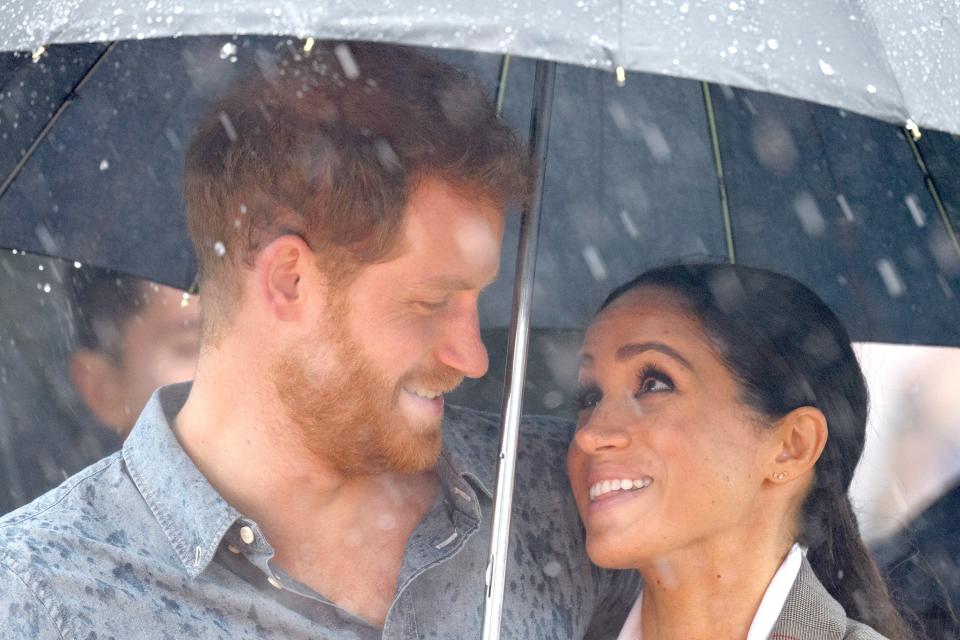 Pregnant Meghan Markle holds umbrella for Prince Harry during a speech about mental health on a recent official visit to Victoria Park in Dubbo, Australia.