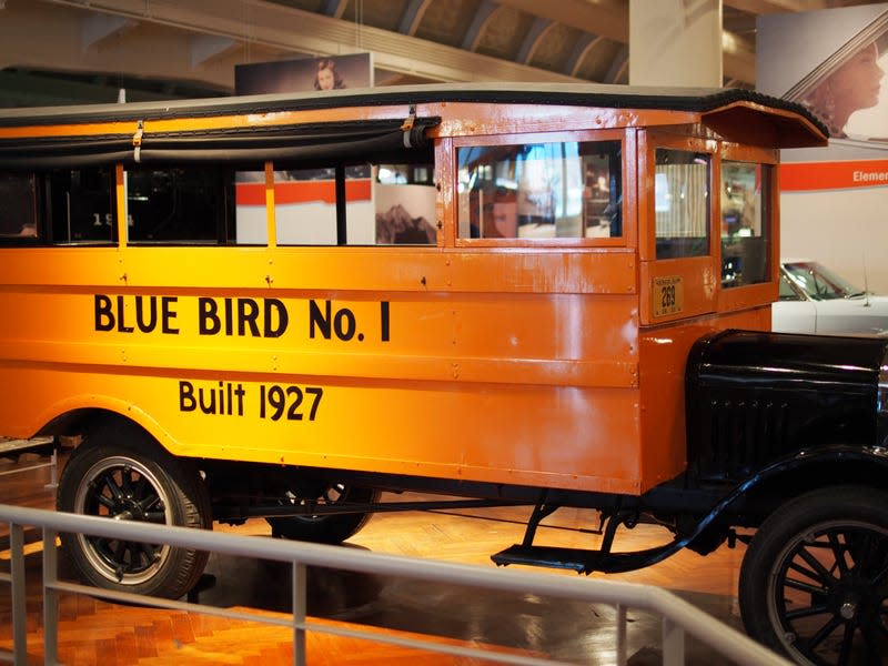 A yellow 1927 school bus with the words Blue Bird No. 1 Built 1927 painted in black on the side.