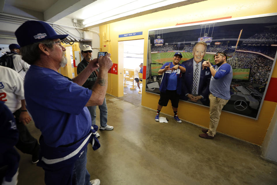 Baseball fans pose for a picture in front of a photo of Vin Scully before the start of an opening day baseball game between the Los Angeles Dodgers and the San Diego Padres, Monday, April 3, 2017, in Los Angeles. (AP Photo/Ryan Kang)