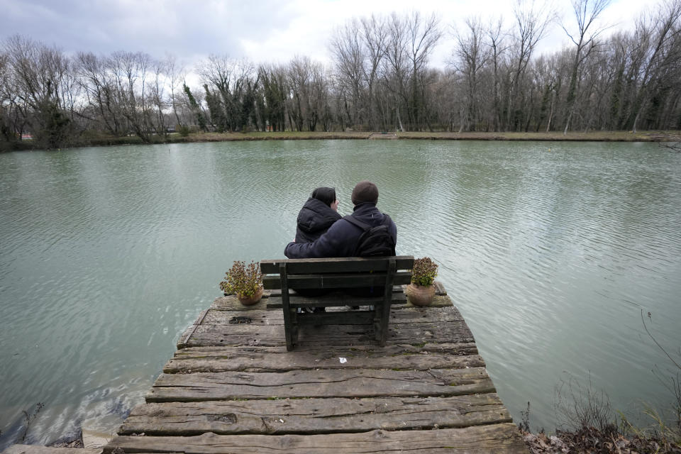 Mariia Vyhivska, from Ukraine, left, and Iurii Kurochkin, from Russia, sit on the bench on the banks of the Ada Safari Lake, in Belgrade, Serbia, Sunday, Feb. 5, 2023. Vyhivska and Kurochkin fell in love before Russia invaded Ukraine, while playing an online video game. To get together, they had to leave their homes and defy hatred generated by war. An estimated 200,000 Russians and some 20,000 Ukrainians have come to Serbia in the past year. (AP Photo/Darko Vojinovic)