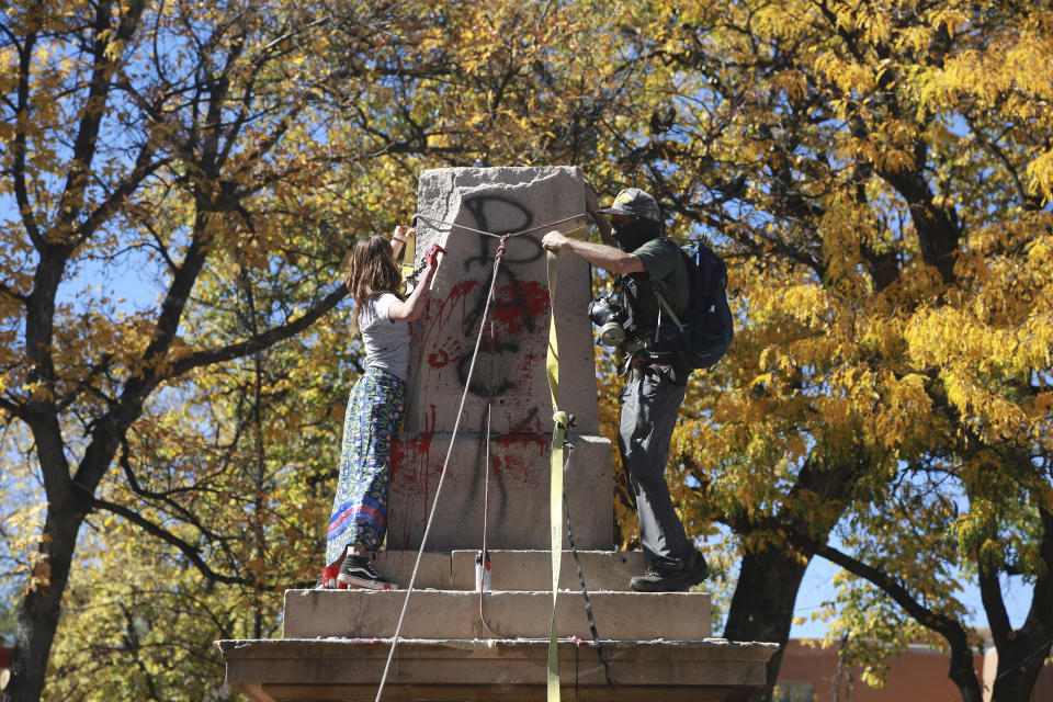 FILE - In this Saturday, Oct. 12, 2020, file photo, demonstrators secure a rope around the centerpiece of a solid stone obelisk before tearing it down in Santa Fe, N.M. The Hispanic cultural association Union Protectiva de Santa Fe sued the city's mayor Wednesday, June 16, 2021, over the destruction of the obelisk by activists last year and plans to move the memorial permanently. The lawsuit argues that the obelisk, which honors Hispanic soldiers that fought and died for the Union in battles with Confederate soldiers and Indigenous tribes, is a protected historical site. (AP Photo/Cedar Attanasio, File)