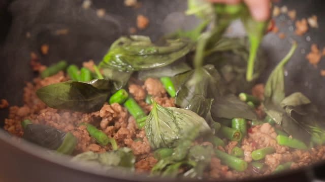 Adding basil leaves to frying pan