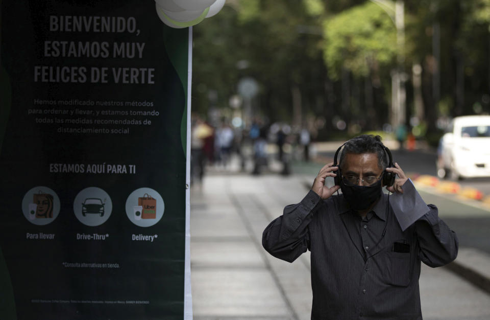 A customer, wearing a protective face mask as a measure to help curb the spread of the new coronavirus, adjusts his headphones prior to entering a coffee shop with an outdoor display panel that reads in Spanish: "Welcome, we are very happy to see you" in Mexico City, Wednesday, July 1, 2020. On a four-color alert level, in which red is the worst and green the best, Mexico City downgraded the city’s alert to “orange” even though it has the country’s largest numbers of infections and deaths. (AP Photo/Fernando Llano)