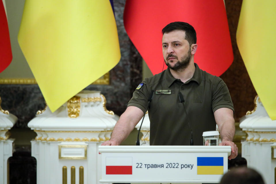 President Volodymyr Zelensky, hands on the podium, surrounded by the flags of Ukraine and Poland, looks solemn. 