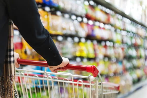 A hand on a shopping cart in a supermarket aisle