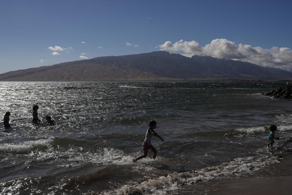 People play in the water along shore, with mountains in the distance