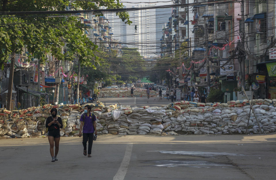 People walk along a deserted road blocked with improvised barricades build by anti-coup protesters to secure a neighborhood in Yangon, Myanmar, Thursday, March 18, 2021. (AP Photo)