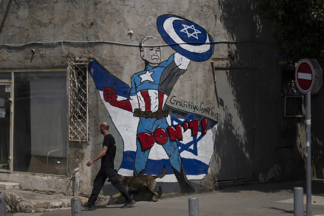 A man walks past a mural depicting Joe Biden as a superhero defending Israel on a street in Tel Aviv. 