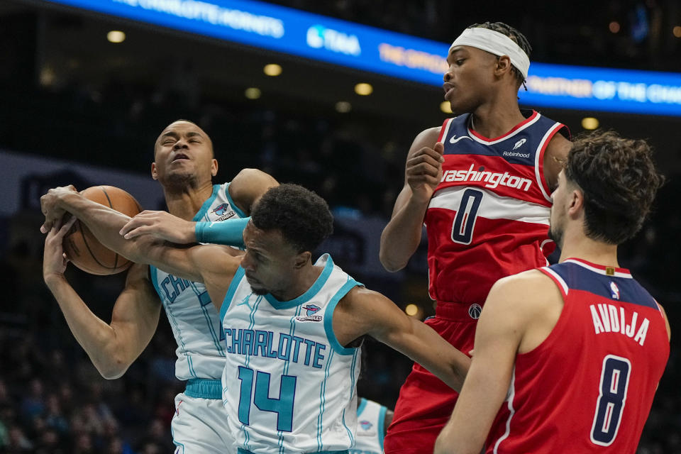 Charlotte Hornets guard Bryce McGowens, left, and guard Ish Smith (14) vie for a rebound as Washington Wizards forward Deni Avdija, right, and guard Bilal Coulibaly look on during the first half of an NBA basketball game on Wednesday, Nov. 22, 2023, in Charlotte, N.C. (AP Photo/Chris Carlson)